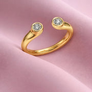 Gold ring with two diamonds on a pink fabric background